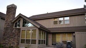 Une maison moderne dotée d’une cheminée en pierre, de grandes fenêtres et d’un patio aménagé avec du mobilier d’extérieur.