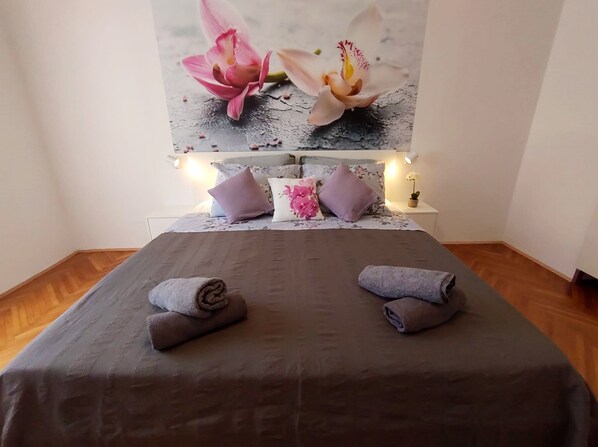 A neatly made bed with two towels, a floral headboard, and a small potted plant on the nightstand.