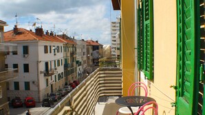 A balcony with a table and chairs, overlooking a street with parked cars and buildings. - Orchidea Apartment Split in the center (Split)