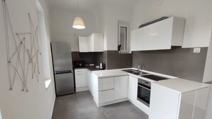 A modern kitchen with white cabinetry, a stainless steel refrigerator, a built-in oven, and a pendant light. - Orchidea Apartment Split in the center (Split)