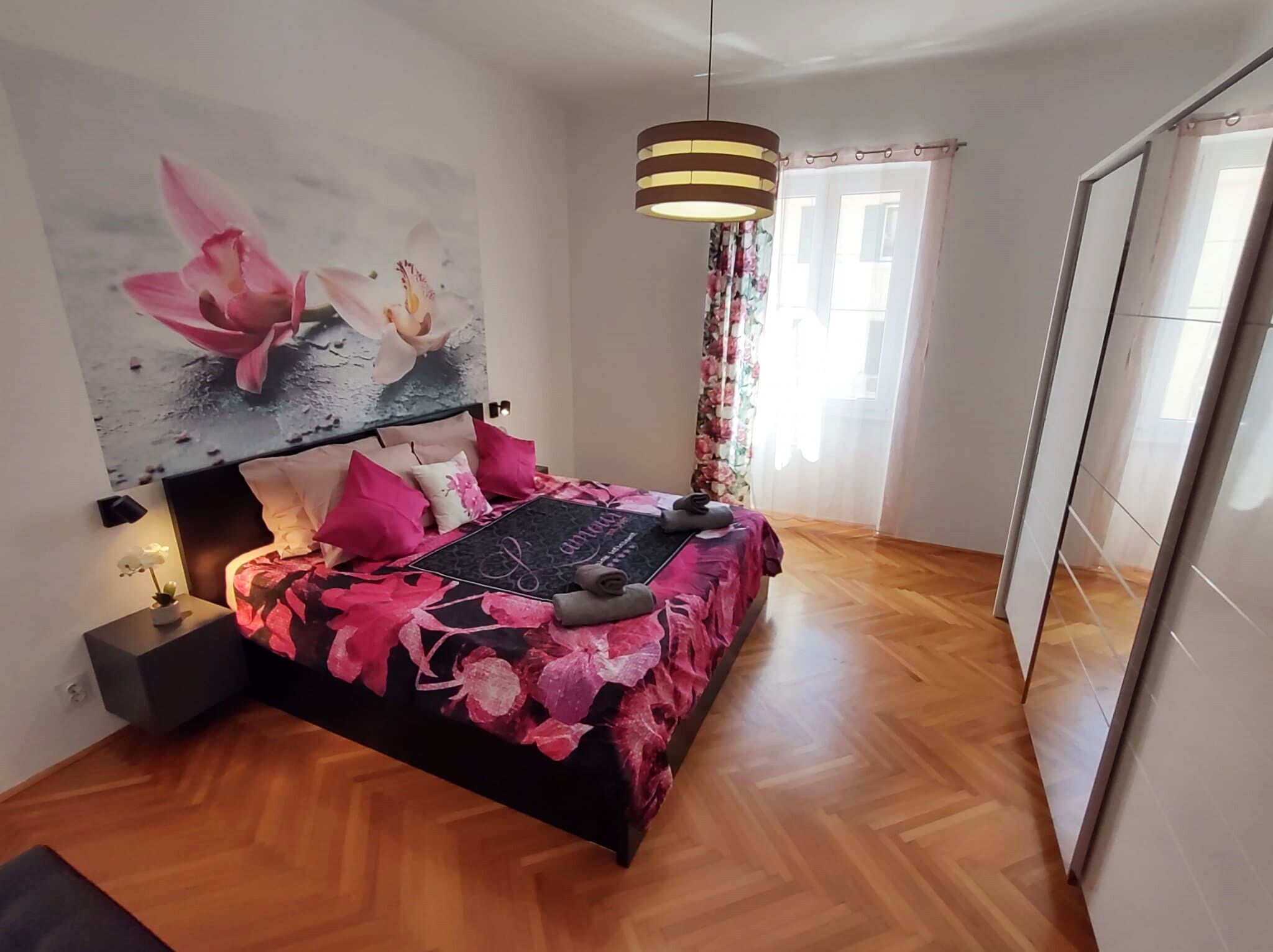 Et moderne soveværelse med en seng, et ophængt kunstværk, et natbord og en hængende lampe.