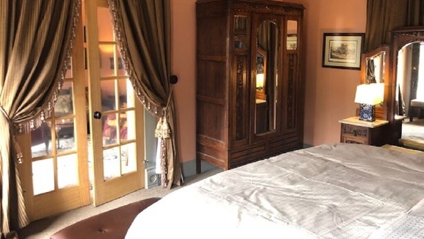 Ein Schlafzimmer mit einem großen Bett, einem Holzschrank, einem Spiegel und einer mit Vorhängen versehenen Tür.