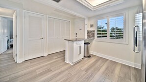 A modern kitchen with white cabinetry, a stainless steel refrigerator, and a window with blinds. - Loggerhead Cay #322 - Sanibel Island Beach View (Sanibel)