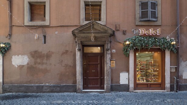 A building with a brown facade, a central entrance with a wooden door, and a shop window displaying items.
