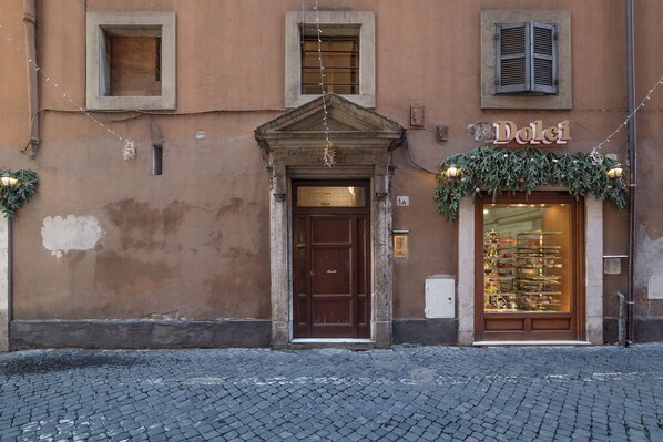 A building with a brown facade, a central entrance with a wooden door, and a shop window displaying items.