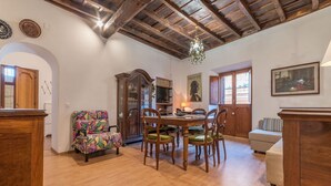 A dining area with a wooden table and chairs, a chandelier, and a painting on the wall.