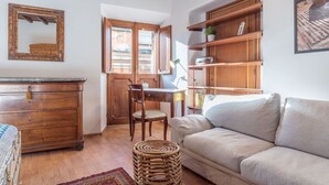 A cozy living room with a wooden dresser, a wicker ottoman, a beige sofa, and a dining area with a wooden table and chairs.