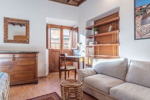 A cozy living room with a wooden dresser, a wicker ottoman, a beige sofa, and a dining area with a wooden table and chairs.