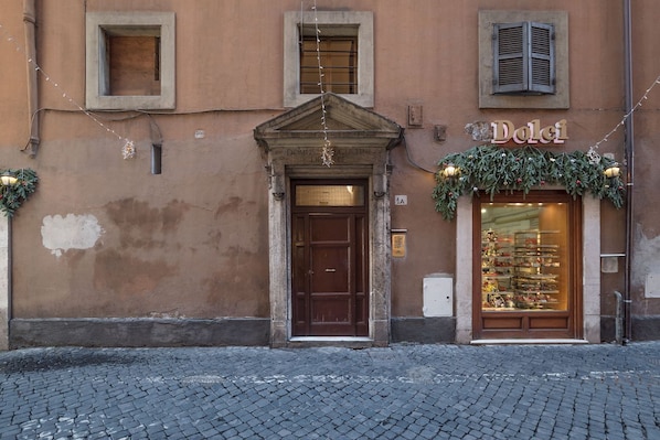 A building with a brown facade, a central entrance with a wooden door, and a shop window displaying items.
