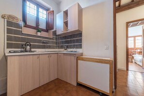 A kitchen with wooden cabinets, a tiled backsplash, a kettle, and a small refrigerator.