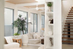 A modern living room with a sofa, a coffee table, a potted plant, and a staircase.