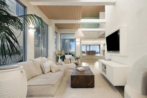Un salon moderne avec un canapé, une table basse, un téléviseur et de grandes fenêtres.
