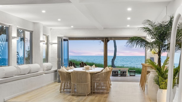 A dining area with a view of the sea, a large window, and a staircase leading to an outdoor deck. - Saltwater Beach House (Yaroomba)