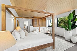 A modern bedroom with a wooden four-poster bed, a large window with a view of greenery, and a white color scheme.