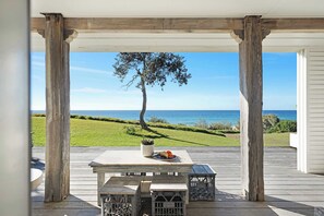 A covered outdoor area with a table and benches, overlooking a grassy landscape and the sea.