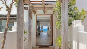 A corridor leading to a room with a view of the sea, wooden pillars, and a white exterior wall. - Saltwater Beach House (Yaroomba)