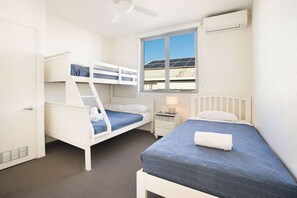 A room with bunk beds, a window with a view, a ceiling fan, and an air conditioning unit.