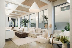 Un soggiorno moderno con un divano componibile, un tavolino da caffè e una poltrona sacco. Sono presenti ampie finestre con piante, una ventola a soffitto e un lampadario.