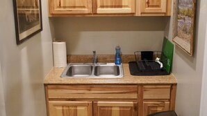 A kitchen with wooden cabinets, a stainless steel sink, a trash can, and a green dish rack.