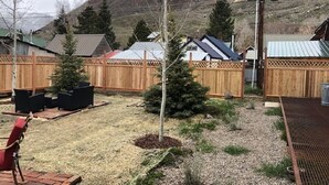 A backyard with a wooden fence, a small tree, and a patio area with outdoor furniture.