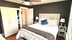 A bedroom with a large bed, a ceiling fan, a wardrobe, and a nightstand with a lamp.