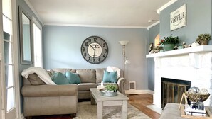 A living room with a beige sofa, a round wall clock, a fireplace, and a blue wall.