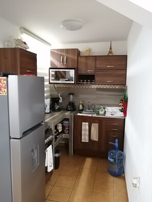 A compact kitchen with wooden cabinets, a refrigerator, a microwave, and a sink. - Charming little house in Tlaquepaque (San Juan)