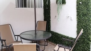 A patio with a round glass table, four chairs, and a large umbrella. - Charming little house in Tlaquepaque (San Juan)