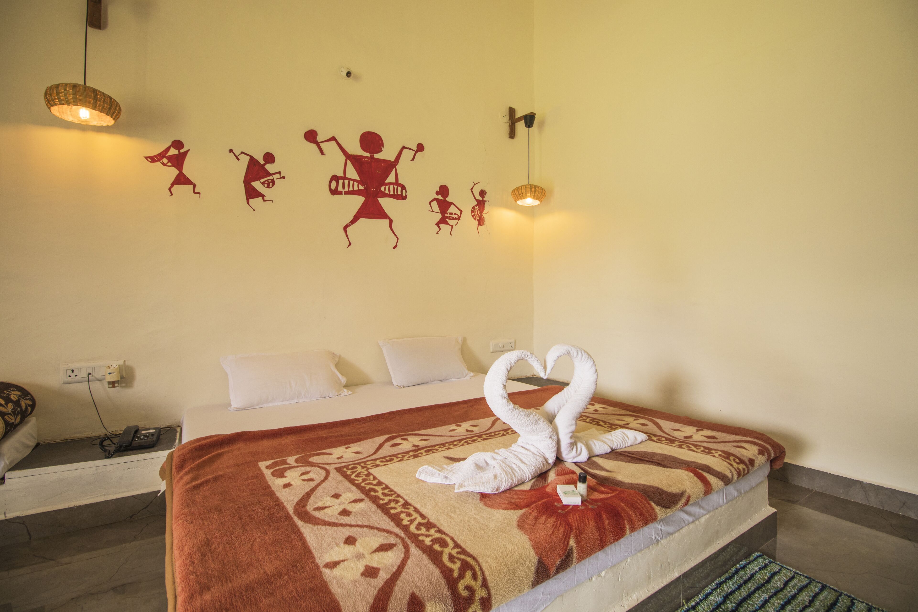 A hotel room with a bed, a wall with red silhouettes of people, a wall-mounted light, and a power outlet.