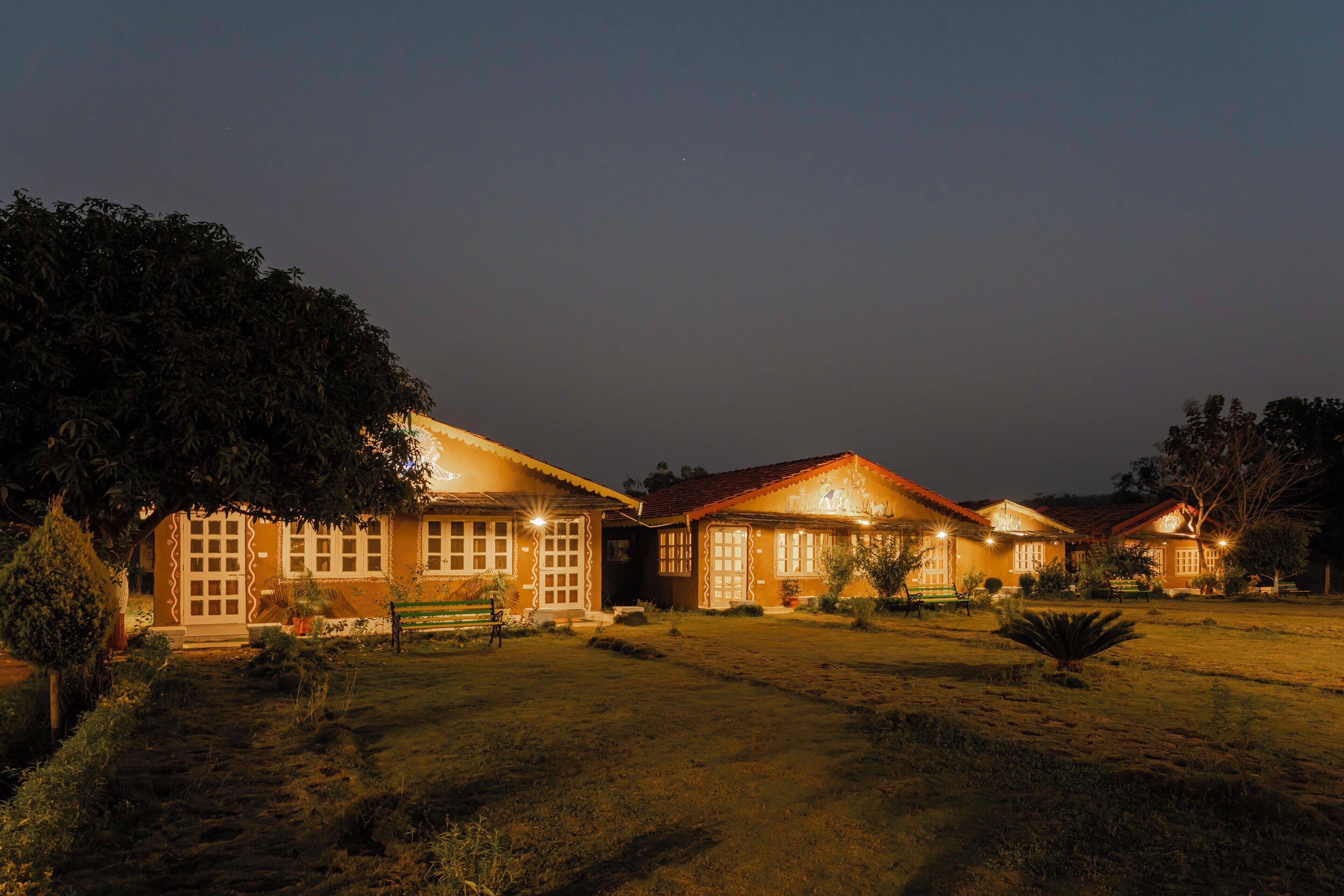 A series of houses with warm lighting, surrounded by greenery and a clear sky.