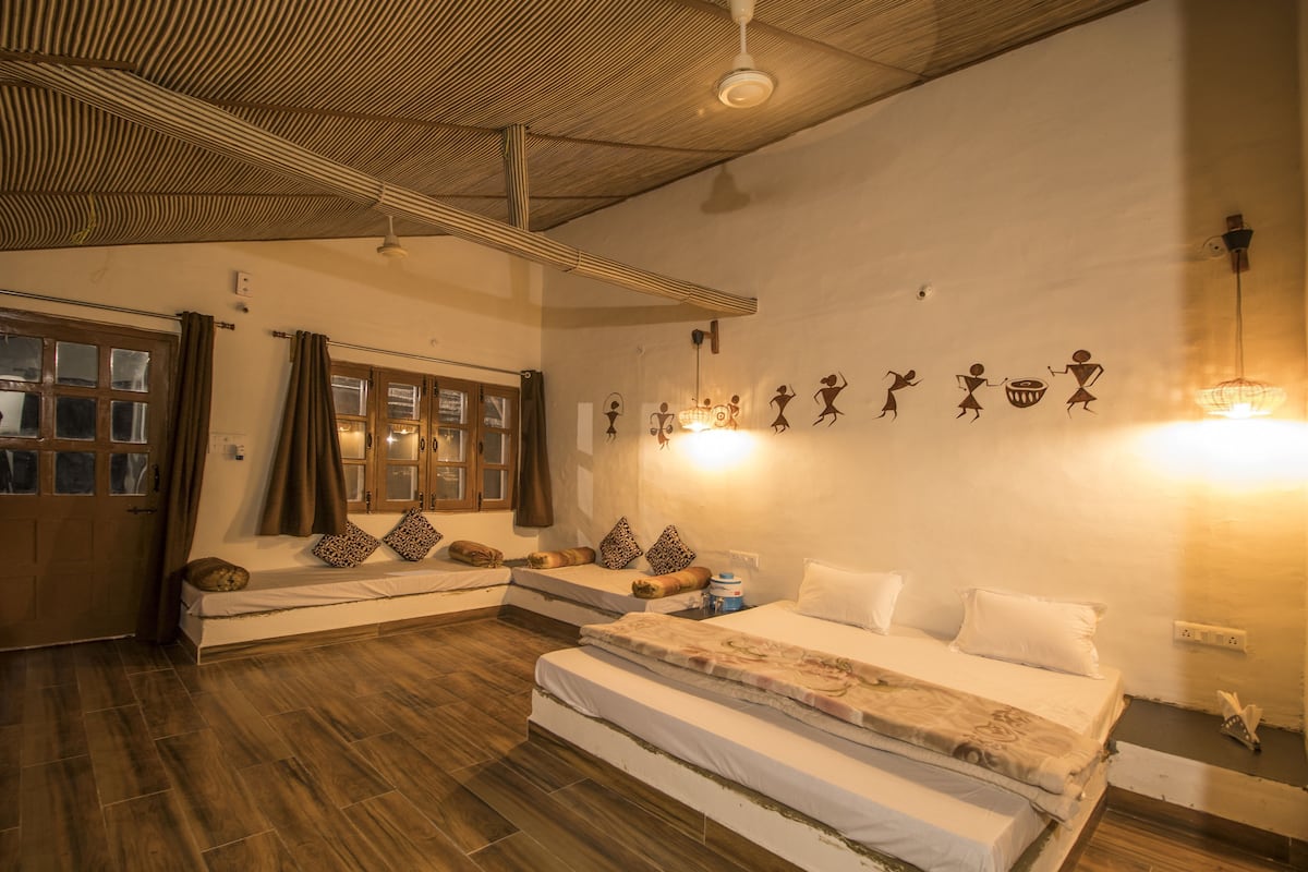 A room with two beds, a wooden ceiling, a window with curtains, wall art, and a light fixture.