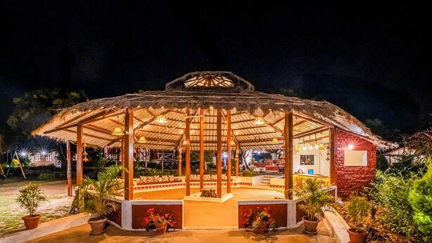 A gazebo-style structure with a thatched roof and wooden pillars, surrounded by potted plants and a brick wall. - Pachmarhi Foothill Cottages by Vanyum (Pipariya)