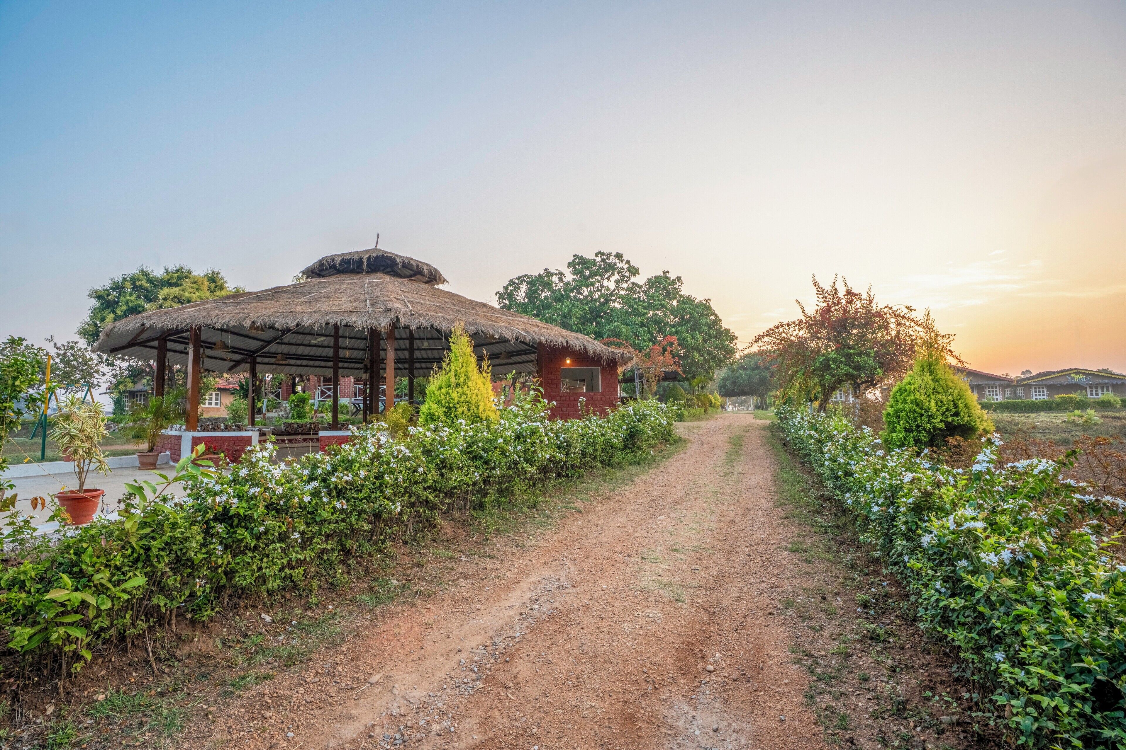 A rustic thatched-roof structure with a dirt path leading to it, surrounded by greenery and trees.