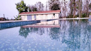 A swimming pool with blue tiles, surrounded by trees and a building with a red roof. - Pachmarhi Foothill Cottages by Vanyum (Pipariya)