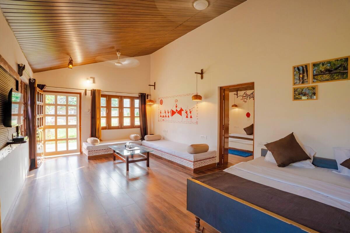 A spacious room with a wooden ceiling, a bed with pillows, a sofa with cushions, a small table, and a wall with framed pictures.