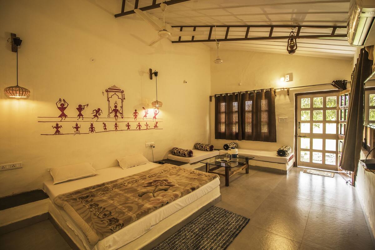 A room with a bed, a sofa, a coffee table, a wall with artwork, and a door leading outside.