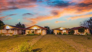 A row of houses with a grassy lawn in front, under a twilight sky. - Pachmarhi Foothill Cottages by Vanyum (Pipariya)