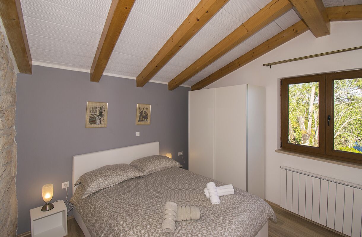 Quarto com cama, luminárias de cabeceira, guarda-roupa e janela com vista para árvores.