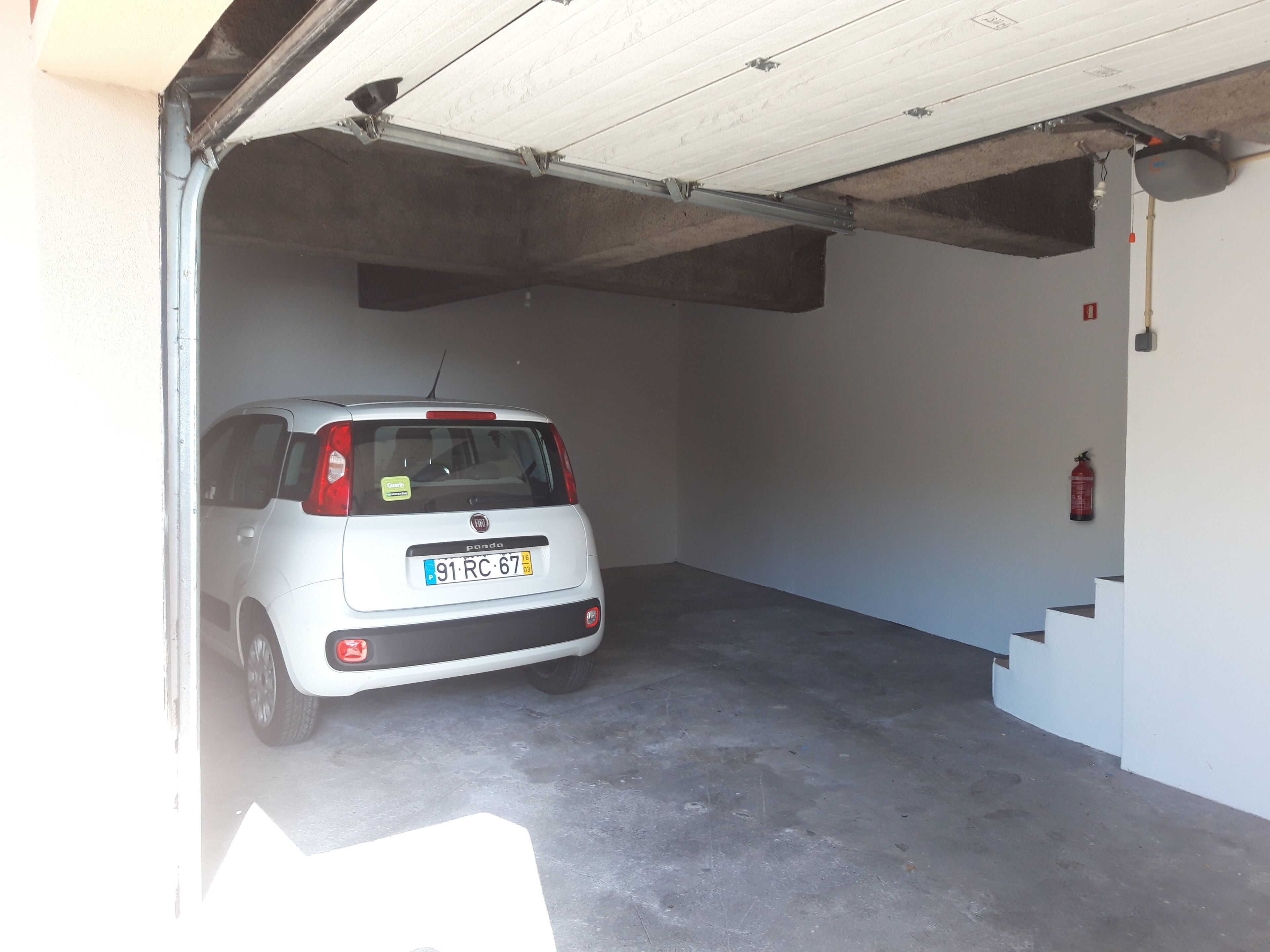A white car parked inside a garage with a concrete floor and a fire extinguisher mounted on the wall.