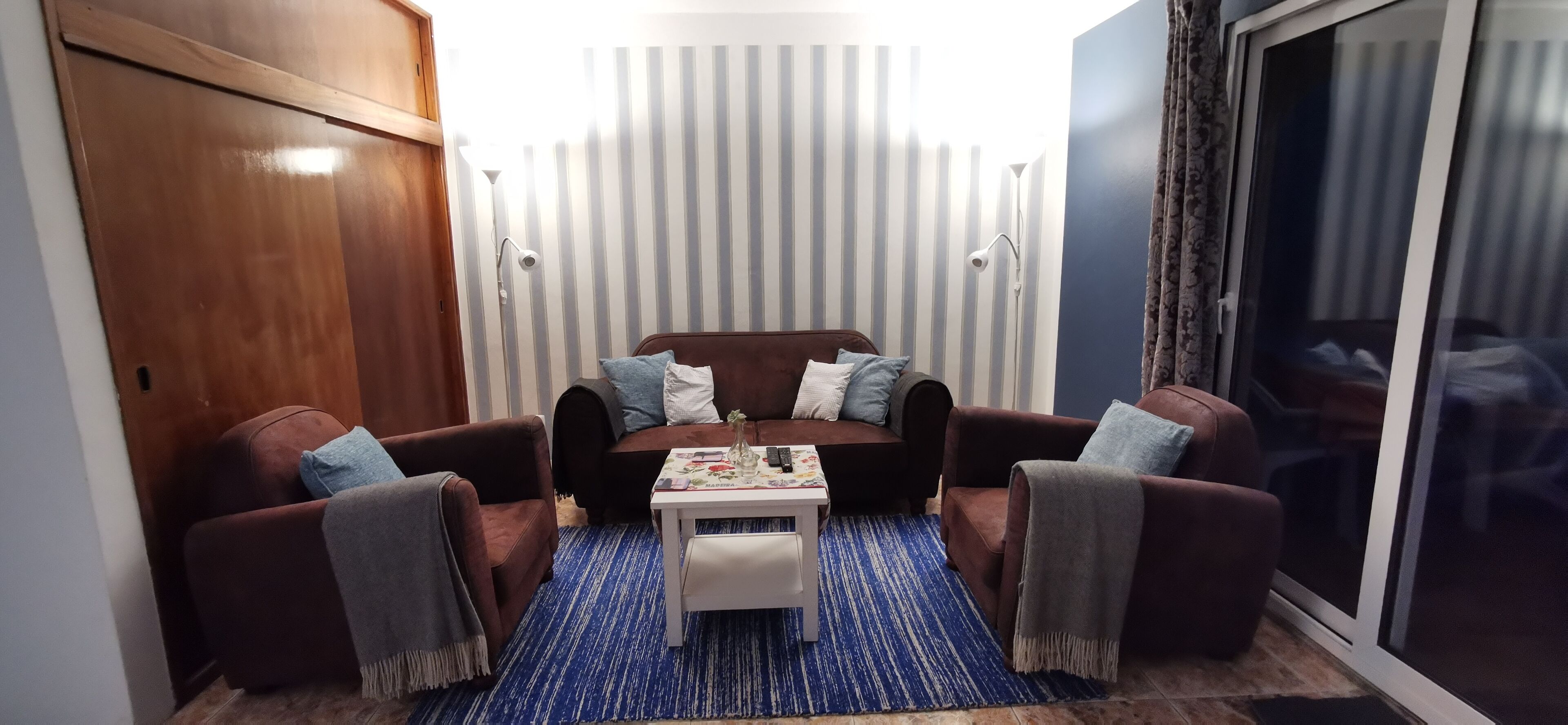 A cozy living room with a brown sofa set, a small white table, and a blue striped rug.