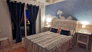 A bedroom with a bed, two bedside tables with lamps, a chair, a window with curtains, and a wall mural. - Villa Tomito, Arco da Calheta (Arco da Calheta)