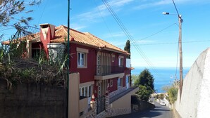 A two-story building with a red facade and a tiled roof, located on a street with a view of the sea. - Villa Tomito, Arco da Calheta (Arco da Calheta)