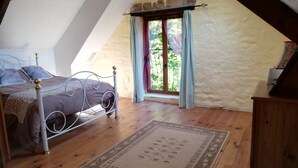 Un dormitorio con techo inclinado, una cama con estructura metálica, un aparador de madera y una ventana con cortinas.