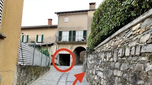 A narrow cobblestone street flanked by buildings with stone walls and a gate. - Top Ferienwohnung - Ticino Lugano (Comano) (Comano)