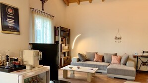 A living room with a sofa, coffee table, and a refrigerator. There is a bookshelf and a small table with a lamp. - Top Ferienwohnung - Ticino Lugano (Comano) (Comano)