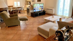 A living room with a television, a sewing machine, and a dining area with a table and chairs. - Top Ferienwohnung - Ticino Lugano (Comano) (Comano)