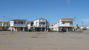 A row of beach houses with balconies, a sandy foreground, and a clear blue sky. - Les Amandines by Interhome (Gruissan)