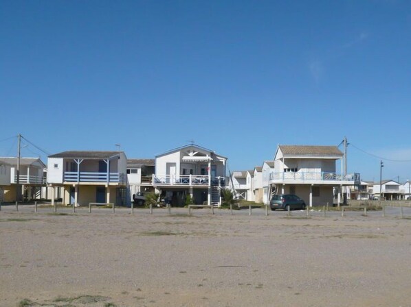 Une rangée de maisons de plage dotées de balcons, un premier plan sablonneux et un ciel bleu dégagé.
