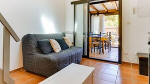A compact living space with a sofa, a small table, and a sliding glass door leading to an outdoor patio area. - Les Amandines by Interhome (Gruissan)