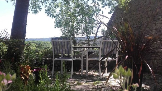 Un espace extérieur aménagé avec deux chaises et une table, entouré de verdure et d’un mur en pierre.